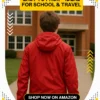 Back view of a teenage boy wearing a red waterproof jacket, heading towards a school building – Best Waterproof Raincoat for Kids Lightweight Hooded Jacket