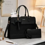 Black leather laptop tote bag for women with a matching wristlet pouch, large tumbler, and adjustable shoulder strap displayed on a modern office desk.