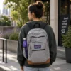 Gray laptop backpack with brown base and side water bottle pocket worn outdoors